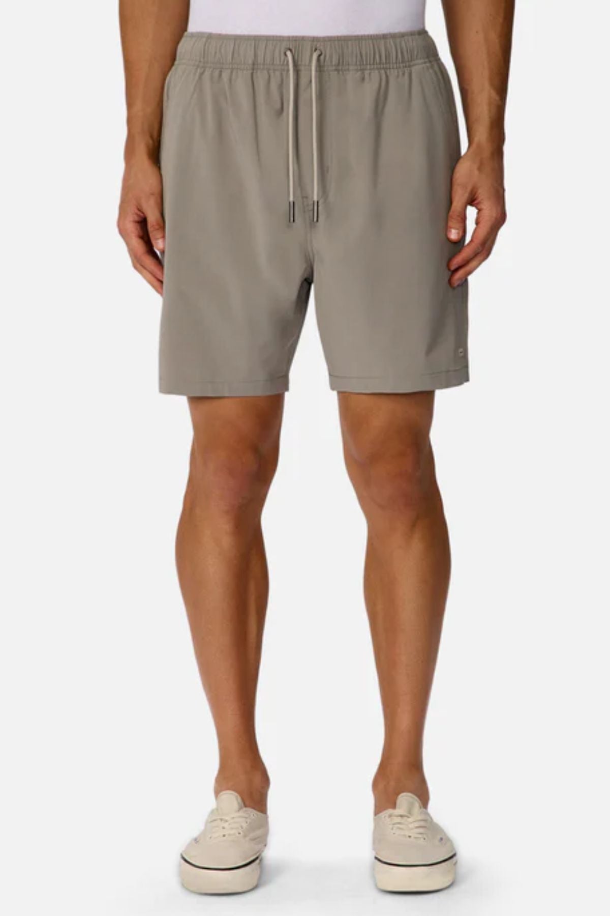 A person wearing Industrie The Barbados Swim Short in light beige, featuring an elastic waistband and drawstring, paired with a white top and beige casual shoes, stands against a plain white background.