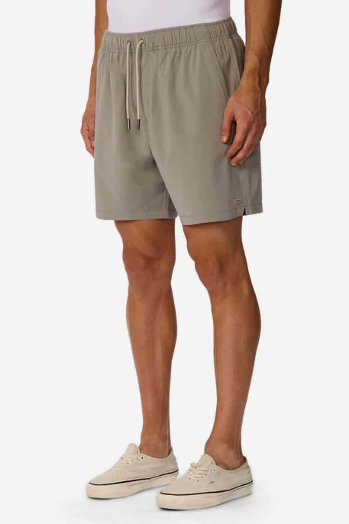 A person wearing Industrie The Barbados Swim Short in light beige, featuring an elastic waistband and drawstring, paired with a white shirt and light sneakers, stands against a plain white background.