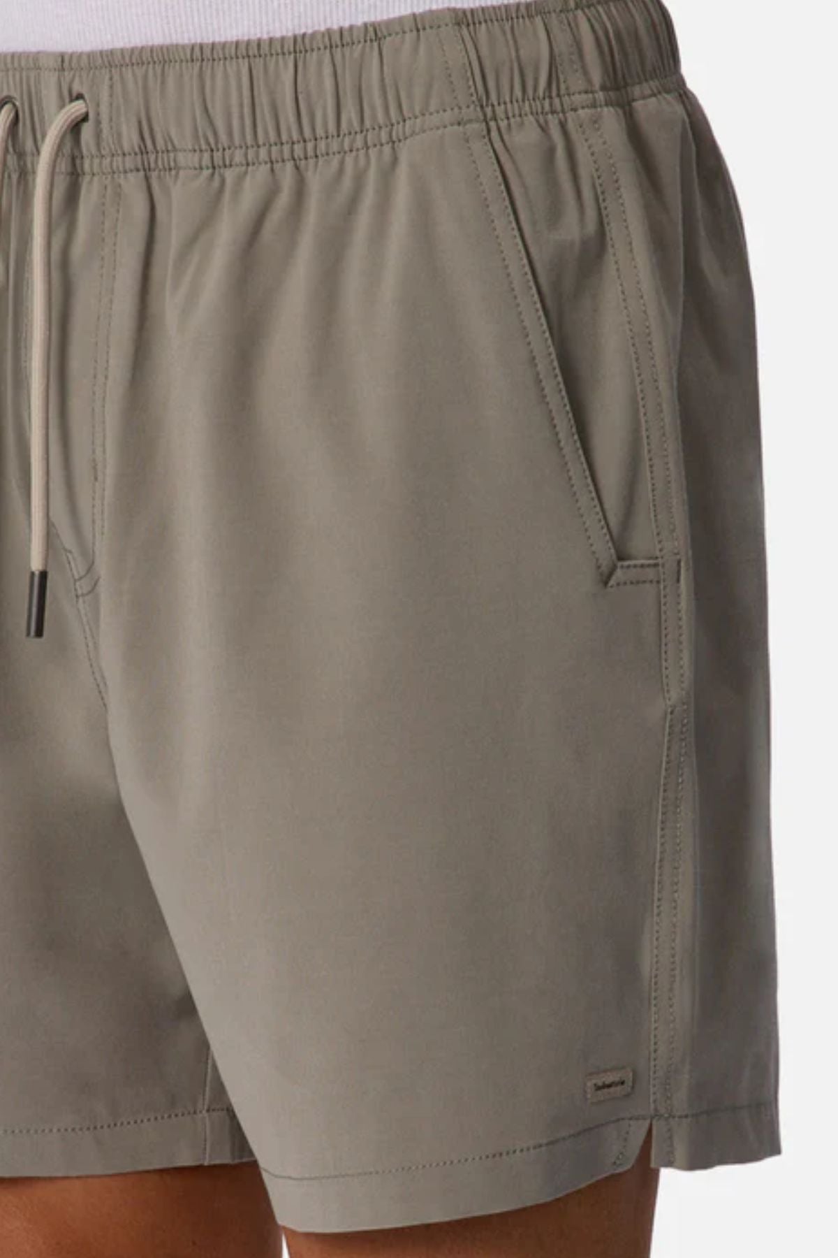 Close-up of a person wearing Industrie The Barbados Swim Short in light gray, featuring side pockets, a fabric logo tag near the hem, quick-dry material, and a cropped fit at the waist and mid-thigh.
