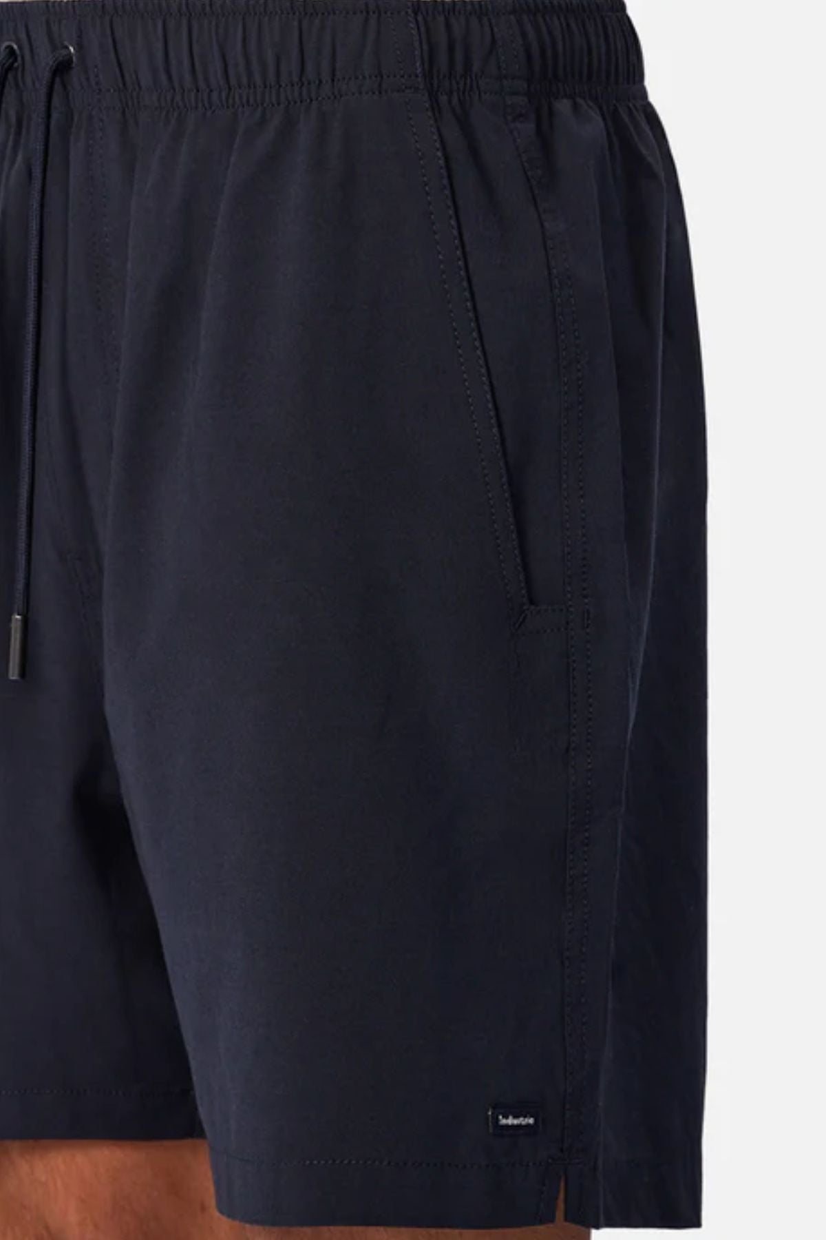 A close-up of a person wearing the Industrie The Barbados Swim Short in dark navy, featuring an elastic waistband and side pockets—ideal men's beachwear, shown waist to mid-thigh against a plain background.