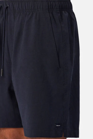 A close-up of a person wearing the Industrie The Barbados Swim Short in dark navy, featuring an elastic waistband and side pockets—ideal men's beachwear, shown waist to mid-thigh against a plain background.