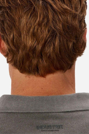 The image features the back of a person with short, wavy brown hair wearing a gray Industrie The Burbank Polo Track shirt against a plain white background.