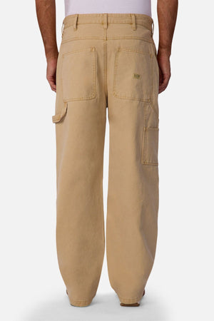 A person wearing Industrie The Carolina Carpenter Pant, featuring loose-fitting, durable cotton fabric with large back pockets and a side tool pocket, shown from the back against a plain white background.