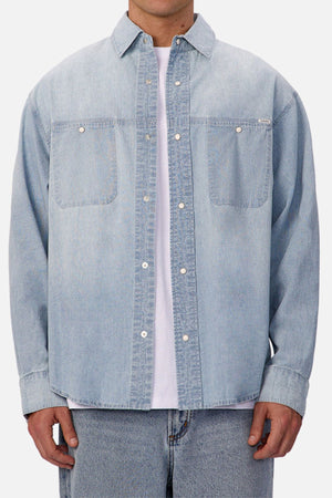 A person wearing the Industrie The Chambray Nebraska Long Sleeve Shirt over a white tee with matching light blue jeans, shown from shoulders to hips against a plain background—a timeless men's workwear look.