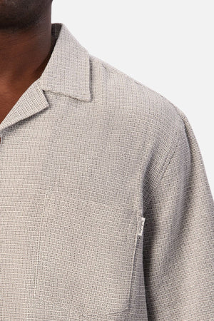 Close-up of a person wearing the Industrie The Check Marbella Short Sleeve Shirt in light gray textured fabric, featuring a collar and chest pocket. The top button is left undone, giving this casual shirt a relaxed feel, with only part of the person’s face and upper torso visible.