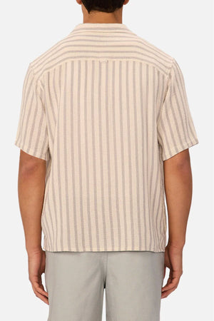 A person is shown from the back wearing the Industrie The Cresta Short Sleeve Shirt, featuring beige and light gray vertical stripes, a camp collar, textured fabric, relaxed fit, and paired with light gray pants.