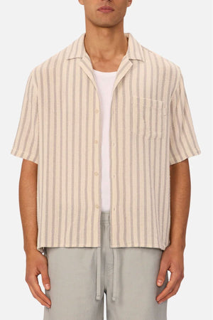 A person wearing the Industrie The Cresta Short Sleeve Shirt in light beige with vertical stripes over a white t-shirt and light gray pants, standing against a plain background.