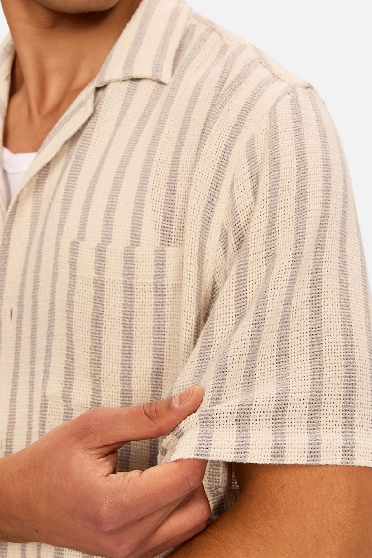 Someone gently pinches the sleeve of the Industrie The Cresta Short Sleeve Shirt, a beige and gray vertical stripe short-sleeve shirt, highlighting its lightweight fabric and textured material.