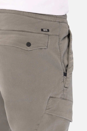 Close-up view of grey Industrie The Defender Combat Pant, highlighting the side pocket with a button closure and a black zipper. A small tag with text is visible above the pocket. The fabric appears to be sturdy and well-stitched, perfect for those seeking durable comfort in their active lifestyle pants.