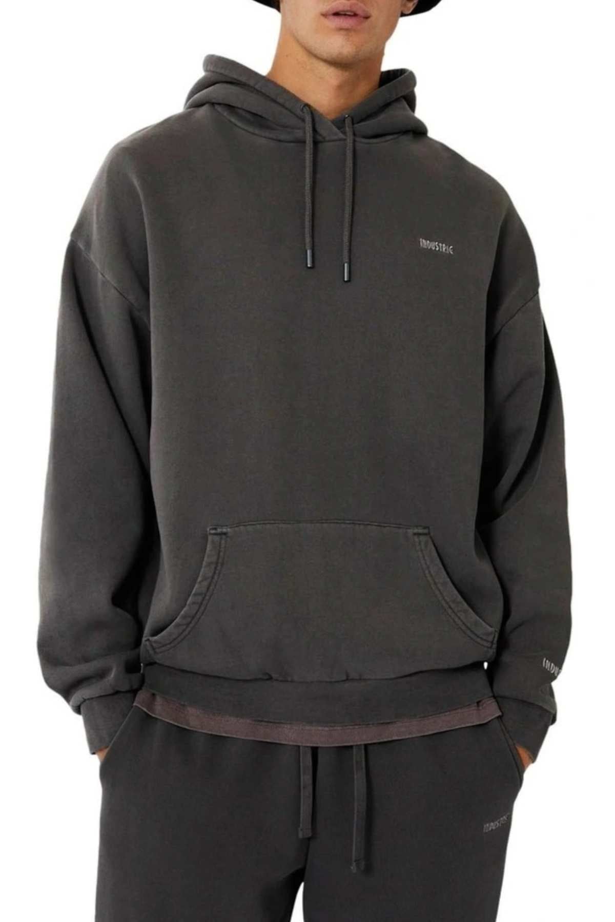 A person wears the Industrie The Del Sur Hoodie in dark gray—an oversized fit with a front pocket, drawstrings, and small chest and sleeve text—paired with matching sweatpants. Their face is partially out of frame.