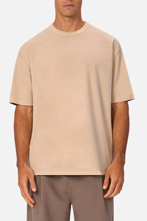 A man wears the Industrie The Del Sur Tee in beige with brown pants, standing against a plain white background.