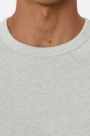 Close-up of a medium-toned person’s neck and upper chest wearing the Industrie The Del Sur Tee in light gray heavyweight fabric, with a visible mole at the center of the neck. The background is plain and uncluttered.