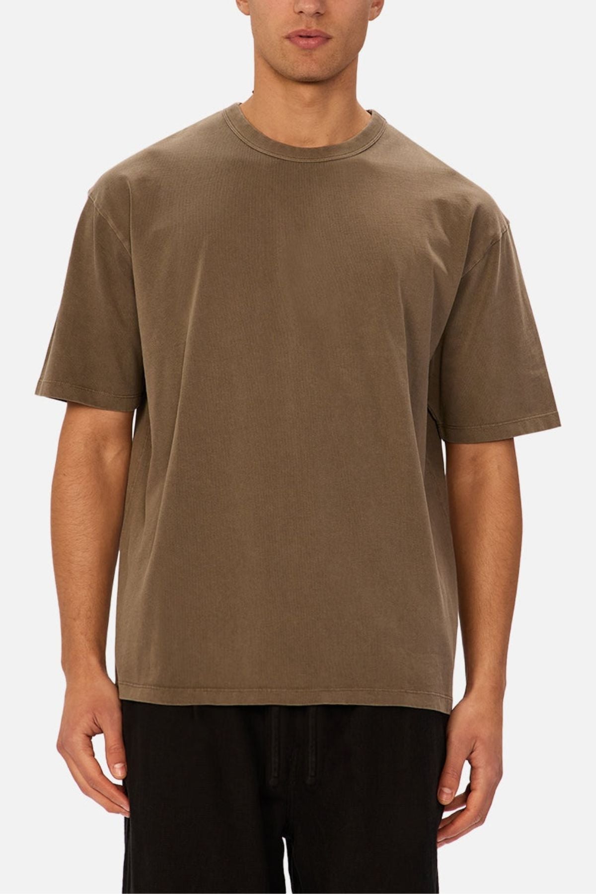 A person stands facing the camera against a plain light background, wearing the Industrie The Del Sur Tee—a loose-fitting heavyweight cotton shirt—paired with black pants.