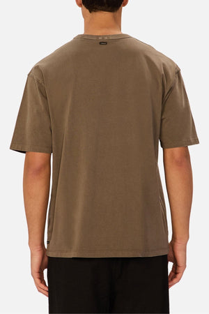 A person is shown from the back against a plain white background, wearing an oversized fit, short-sleeve brown Industrie The Del Sur Tee made from heavyweight cotton and black pants.