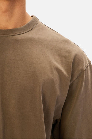 A close-up of a person wearing an oversized, plain olive green Industrie The Del Sur Tee made from heavyweight cotton, highlighting the neck, shoulder, and upper chest against a light background.