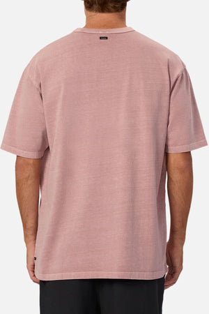 A man is seen from the back wearing the Industrie The Del Sur Tee in an oversized fit and light pink color, made of heavyweight fabric. The short-sleeved tee has a simple design with no visible logos or graphics and is paired with black pants.