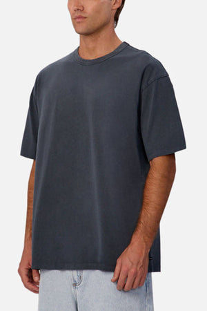 A man wearing the Industrie The Del Sur Tee in dark gray and light blue jeans stands against a plain light background.