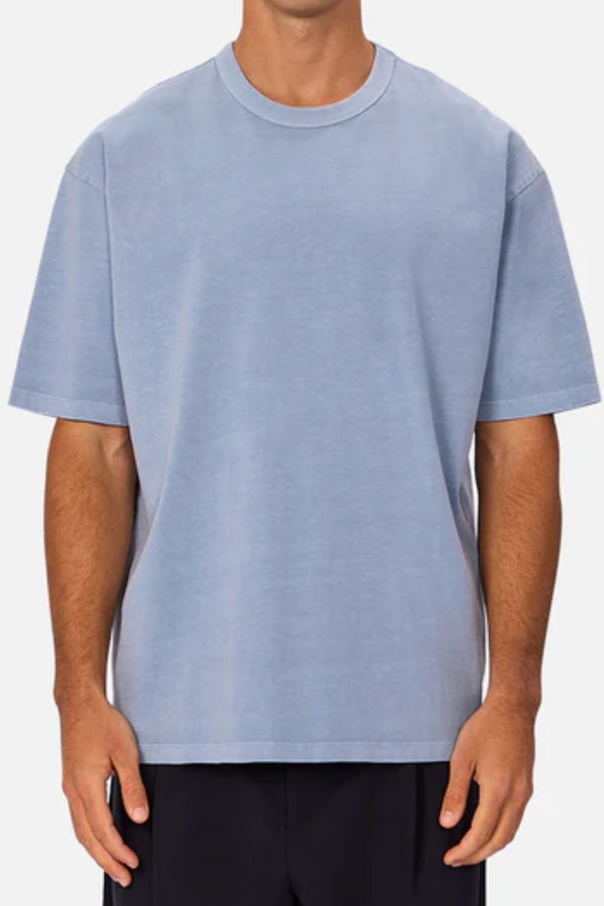 A person, head not visible, wears an oversized Industrie The Del Sur Tee in light blue with black pants, standing against a plain light background.