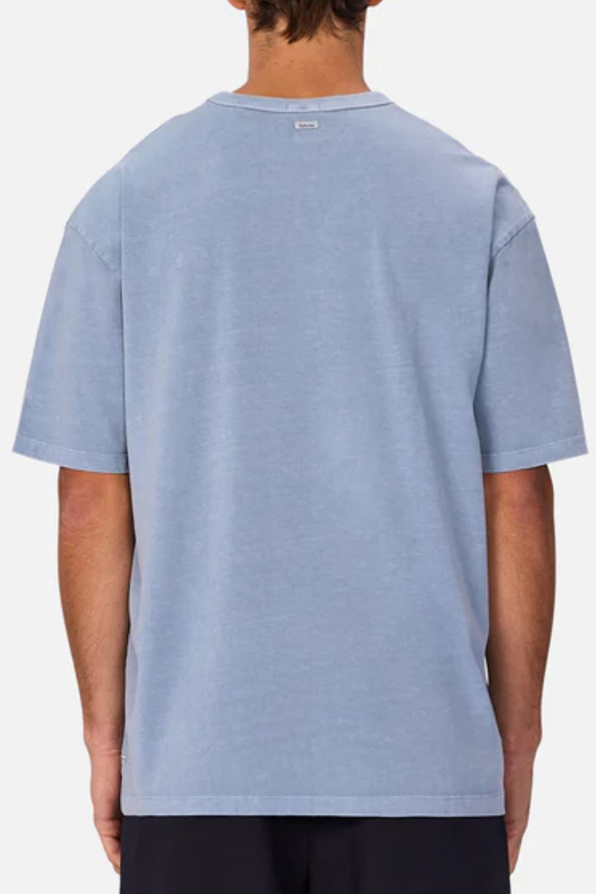 A person is seen from behind wearing an oversized light blue Industrie The Del Sur Tee with black pants, standing against a plain light background.