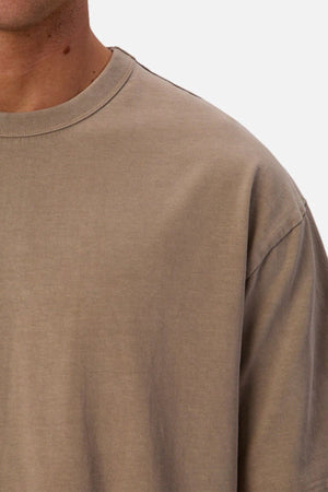 Close-up of a person wearing the Industrie The Del Sur Tee in light brown. The image shows only the shoulder, chest, and part of the neck and face against a plain, light background.