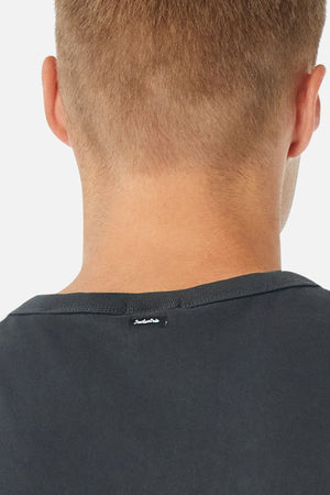 Close-up of the back of a person's head with short light brown hair, wearing the Industrie The Del Sur Tee. This black, oversized 100% cotton T-shirt features a small white label near the collar, shown against a plain white background.