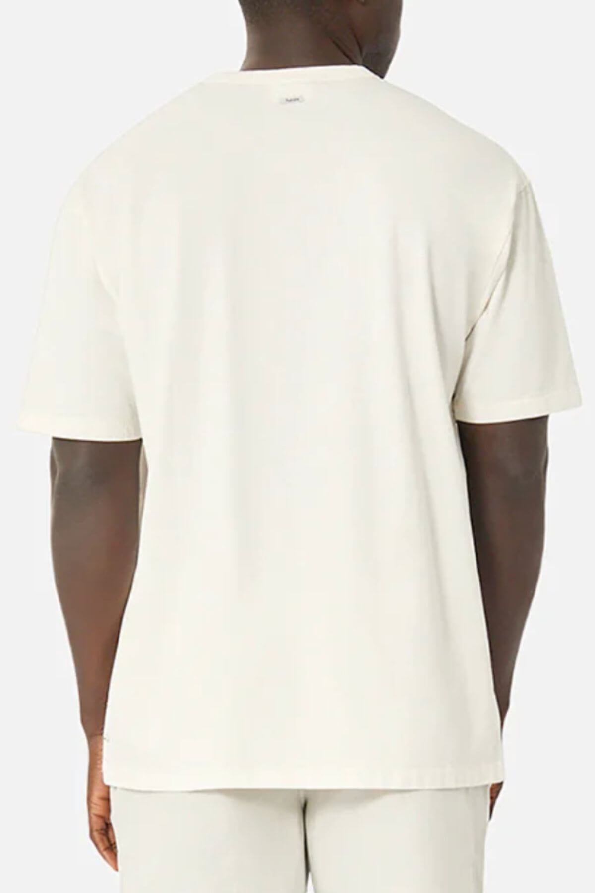 A person stands against a neutral background wearing an Industrie The Del Sur Tee, a plain, light-colored oversized T-shirt made from 100% cotton. It pairs with matching pants. The shirt is loose-fitting, and the fabric looks incredibly soft.