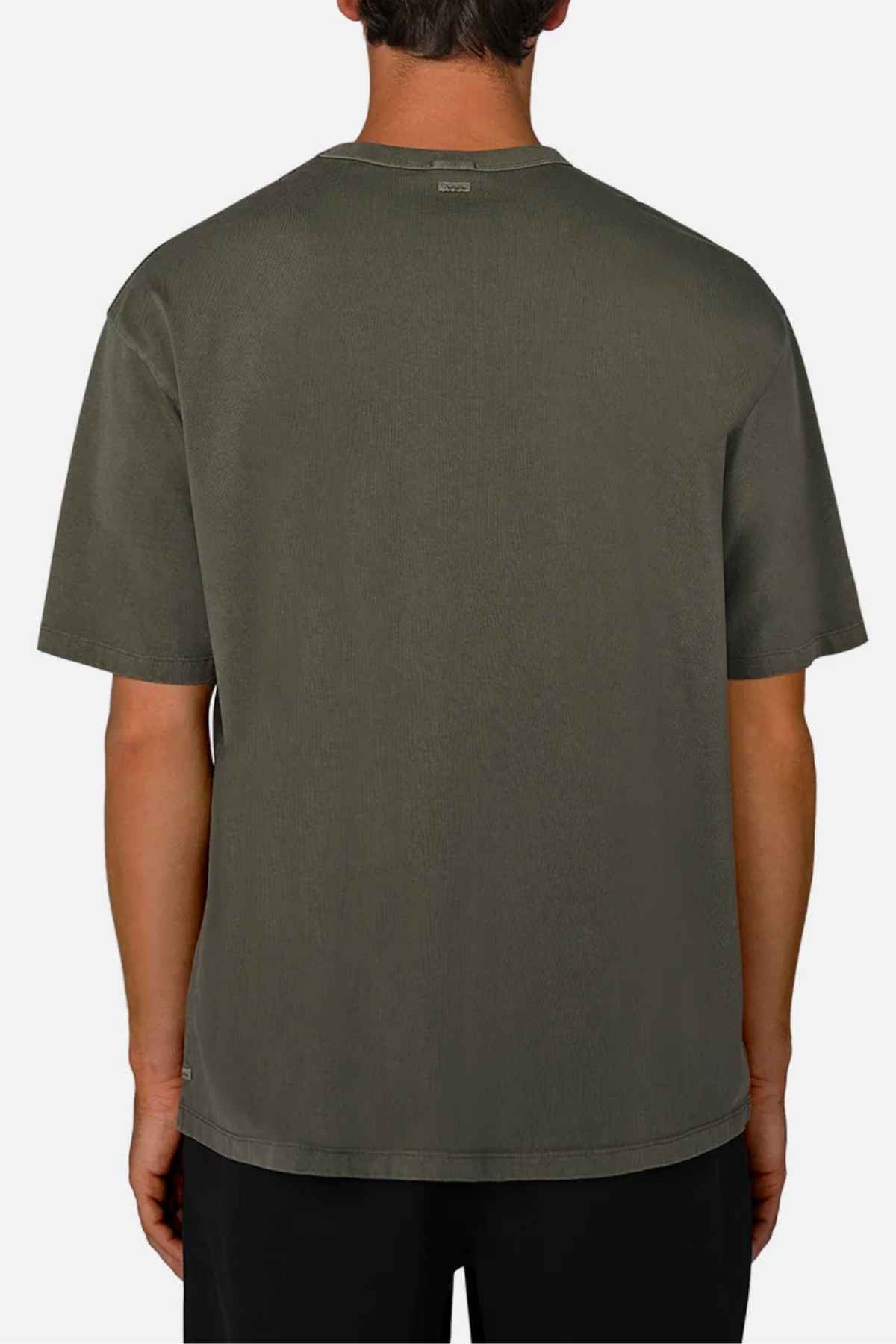 An individual is wearing the Industrie The Del Sur Tee in an oversized fit and olive green, positioned with their back to the camera. Made from 100% cotton, this short-sleeved shirt complements black pants effortlessly. The backdrop is a solid light gray color, highlighting a casual yet stylish appearance.