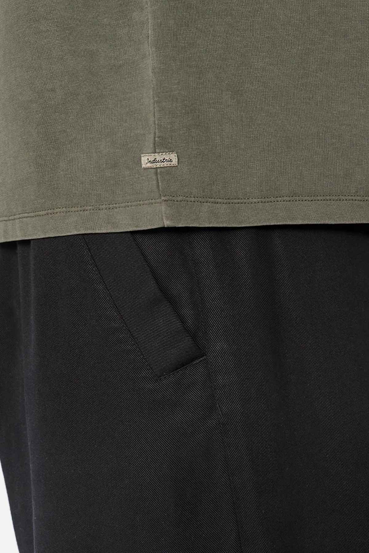 Close-up image showcasing the bottom of an olive-green, oversized Industrie The Del Sur Tee with a small tag on the seam. Crafted from 100% cotton, this stylish piece pairs perfectly with black pants.