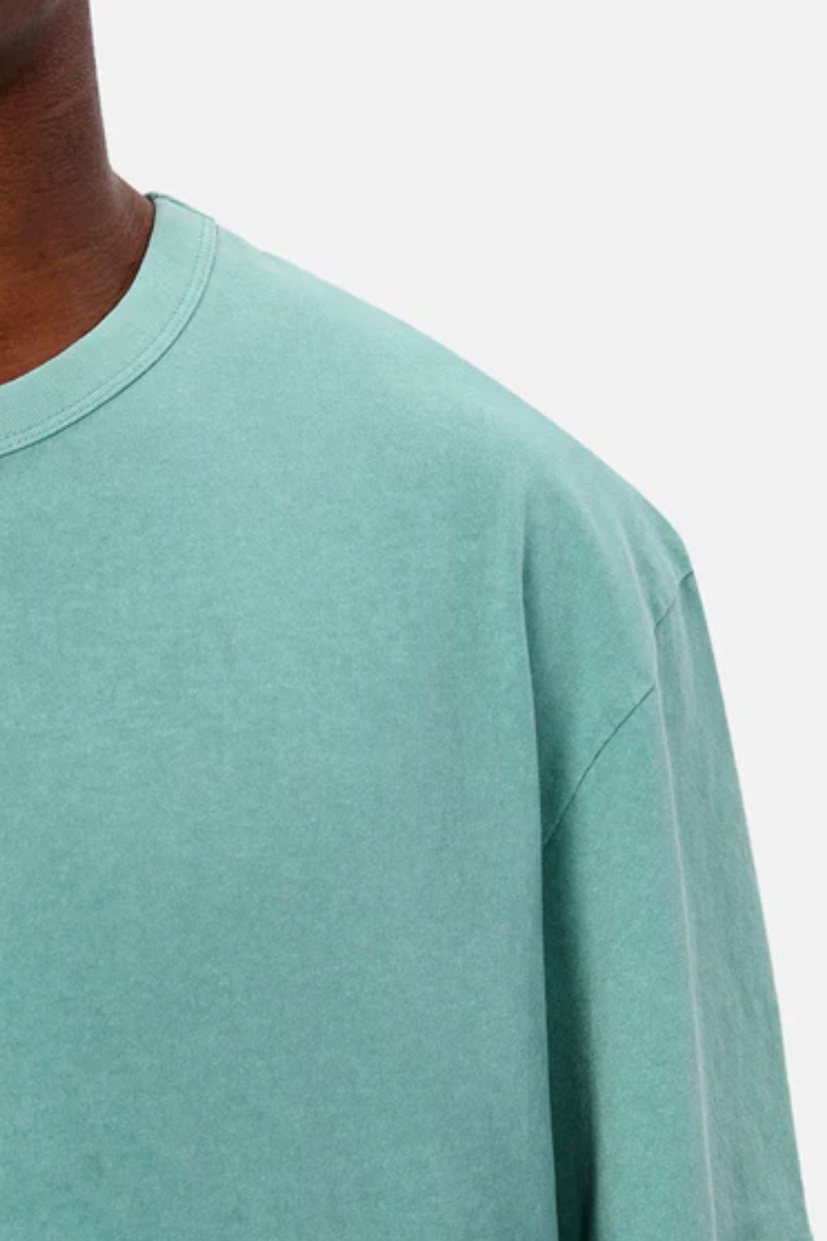 Close-up of a person wearing the Industrie The Del Sur Tee in light teal. The image highlights the oversized t-shirt’s upper left section and shoulder against a plain, light background.