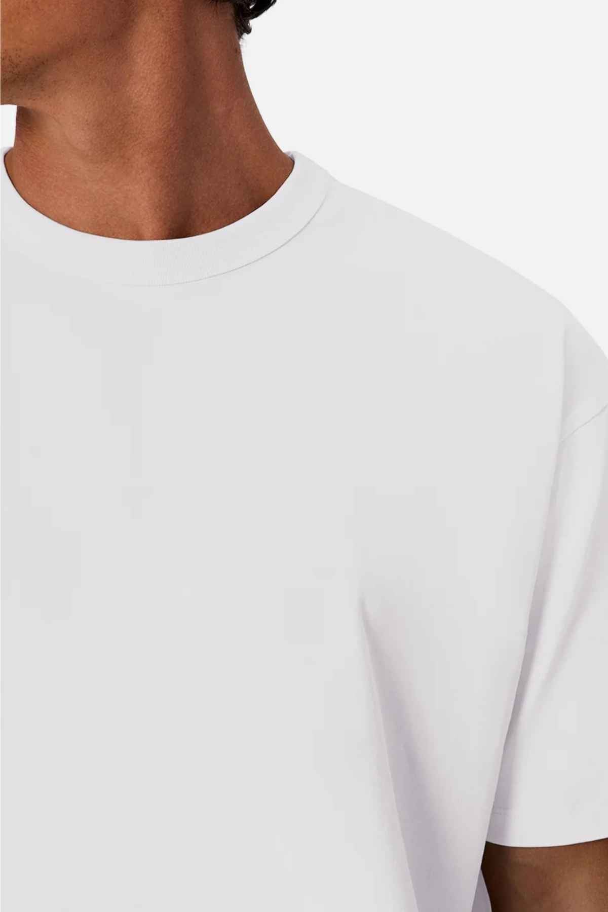 The image features an individual donning the Industrie The Del Sur Tee in a crisp white shade, captured from the neck down, highlighting just a portion of the shoulder and chest against a white backdrop. Crafted from 100% cotton, this tee offers an airy feel perfect for any occasion.