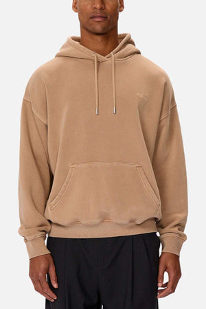 Someone wearing the Industrie The Del Sur Washed Hoodie, an oversized, cozy beige fit with a front pocket and drawstrings. It features a subtle logo on the upper left. Paired with black pants against a plain white background, it completes the comfortable aesthetic.