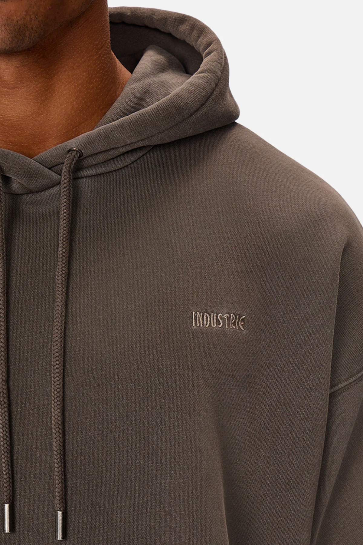 A person wears the Industrie The Del Sur Washed Hoodie in dark gray, featuring sleek "INDUSTRIE" embroidery on the chest. With the hood down and drawstrings hanging in front against a white backdrop, its subtle acid wash adds modern edge to the classic design.