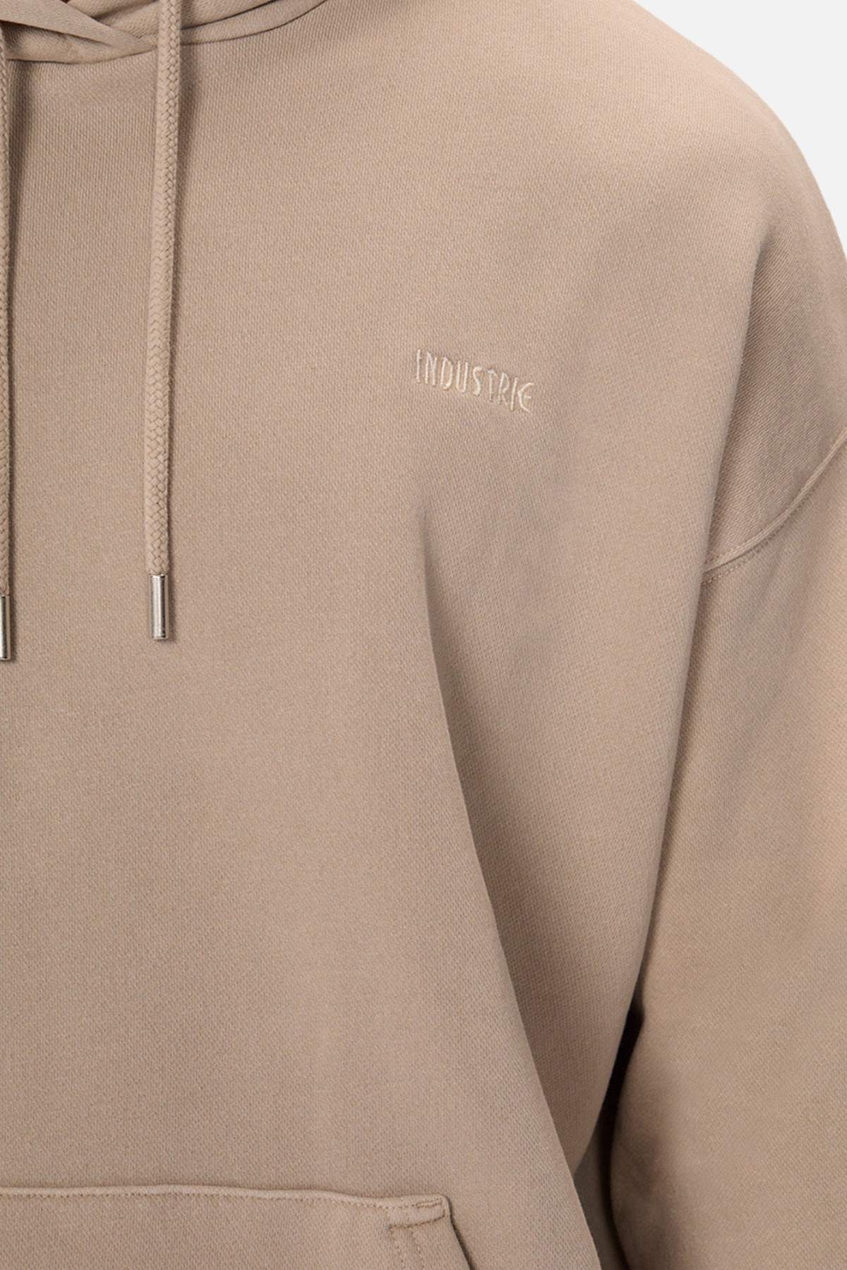 A person wears an oversized, soft beige hoodie with drawstrings. The Del Sur Washed Hoodie features "INDUSTRIE" embroidered subtly on the chest, offering a cozy and inviting fit.