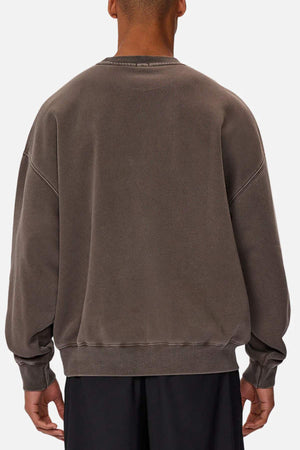 A person is shown from the back wearing the Industrie The Del Sur Washed Sweat in an oversized, faded brown style with dropped shoulders and ribbed cuffs and hem, paired with black pants against a plain light background.