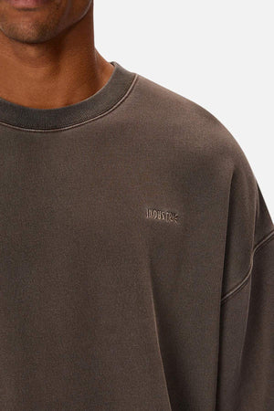 A close-up of a person wearing the Industrie The Del Sur Washed Sweat, an oversized dark grey acid wash jumper with "INDUSTRIE" embroidered on the chest, against a plain white background.