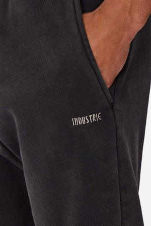 Close-up of a person wearing Industrie The Del Sur Washed Track Pant, featuring an elasticated drawstring waist and their hand in the pocket. "INDUSTRIE" is embroidered in small white letters near the pocket.