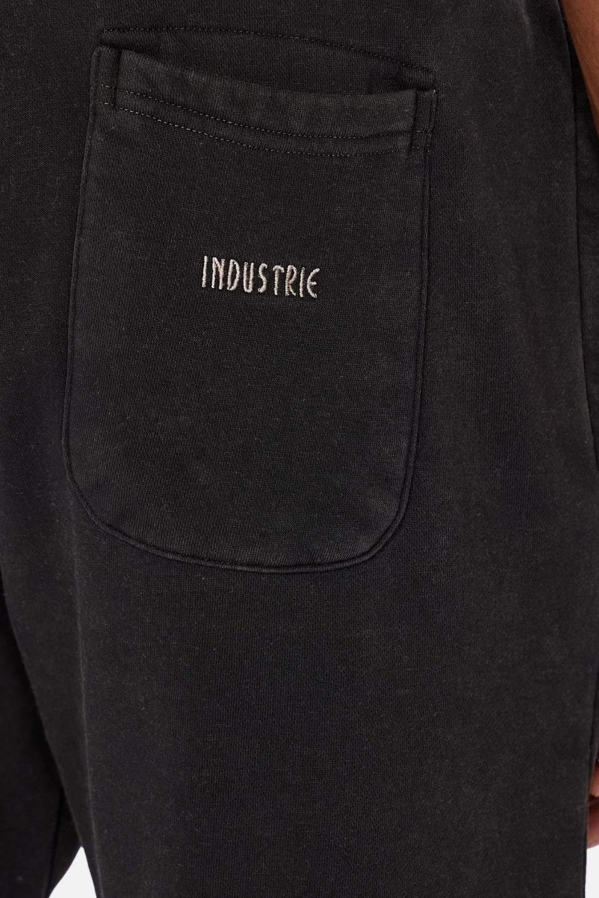Close-up of a black fabric pocket with "INDUSTRIE" in white embroidery, likely from Industrie The Del Sur Washed Track Pant, suggesting casual style with possible elasticated drawstring waist or acid wash.