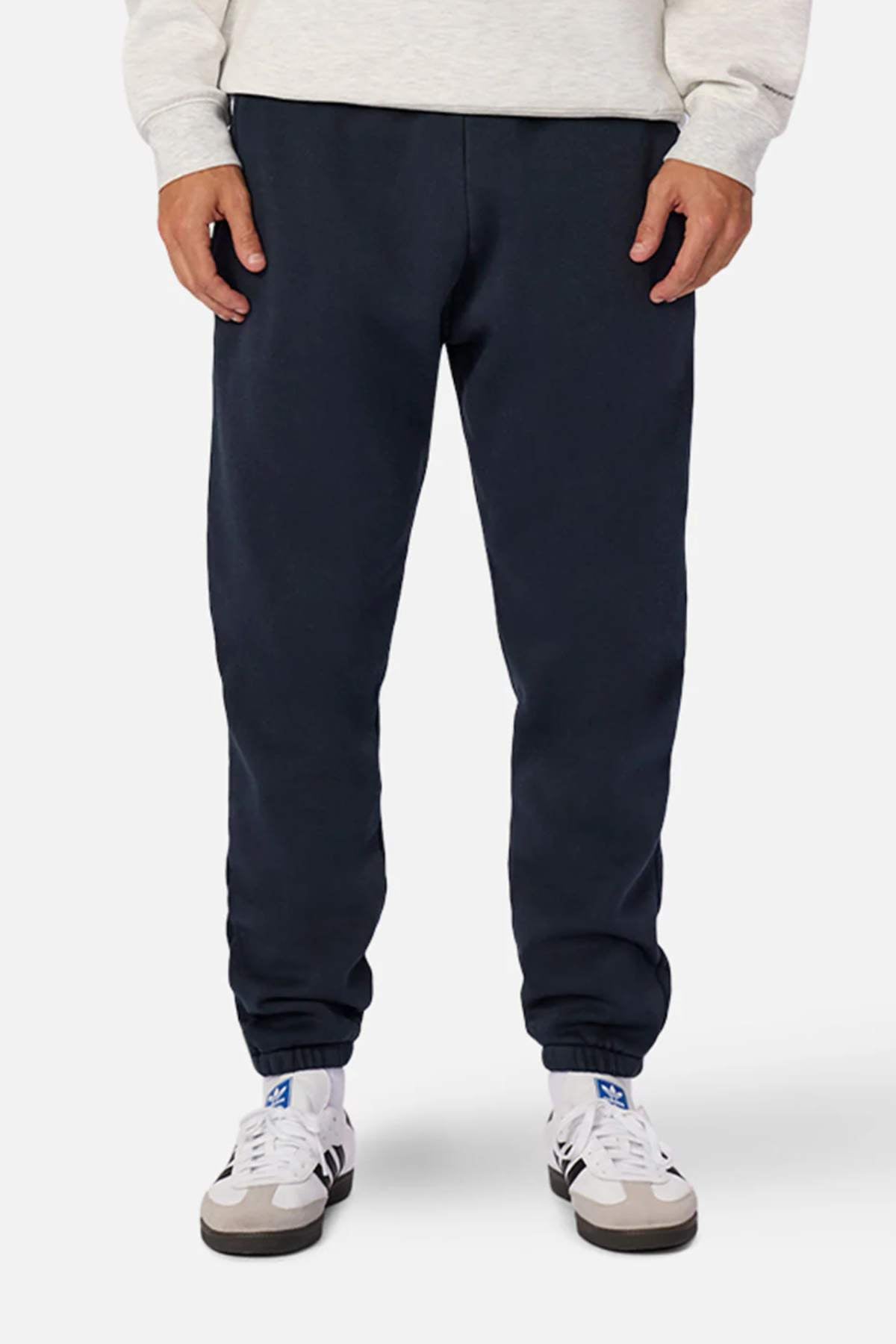 A person is standing against a plain background, wearing an oversized light-colored sweatshirt and the Industrie The Del Sur Washed Track Pant, which are dark blue sweatpants featuring an elasticated drawstring waist. The person is also wearing white athletic shoes with blue accents. The image showcases the lower half of the person's body, from the waist down to their feet.