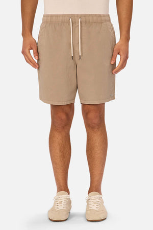 A person wears Industrie The Dublin Short in tan, a light shirt, and beige sneakers, standing against a plain white background.