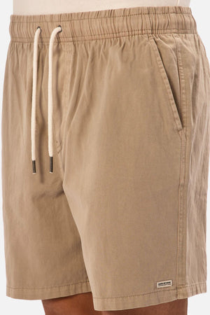A close-up of a person wearing Industrie The Dublin Short, light brown with an elastic waist, pockets, a small stitched label near the hem, and white drawstrings with metal tips.