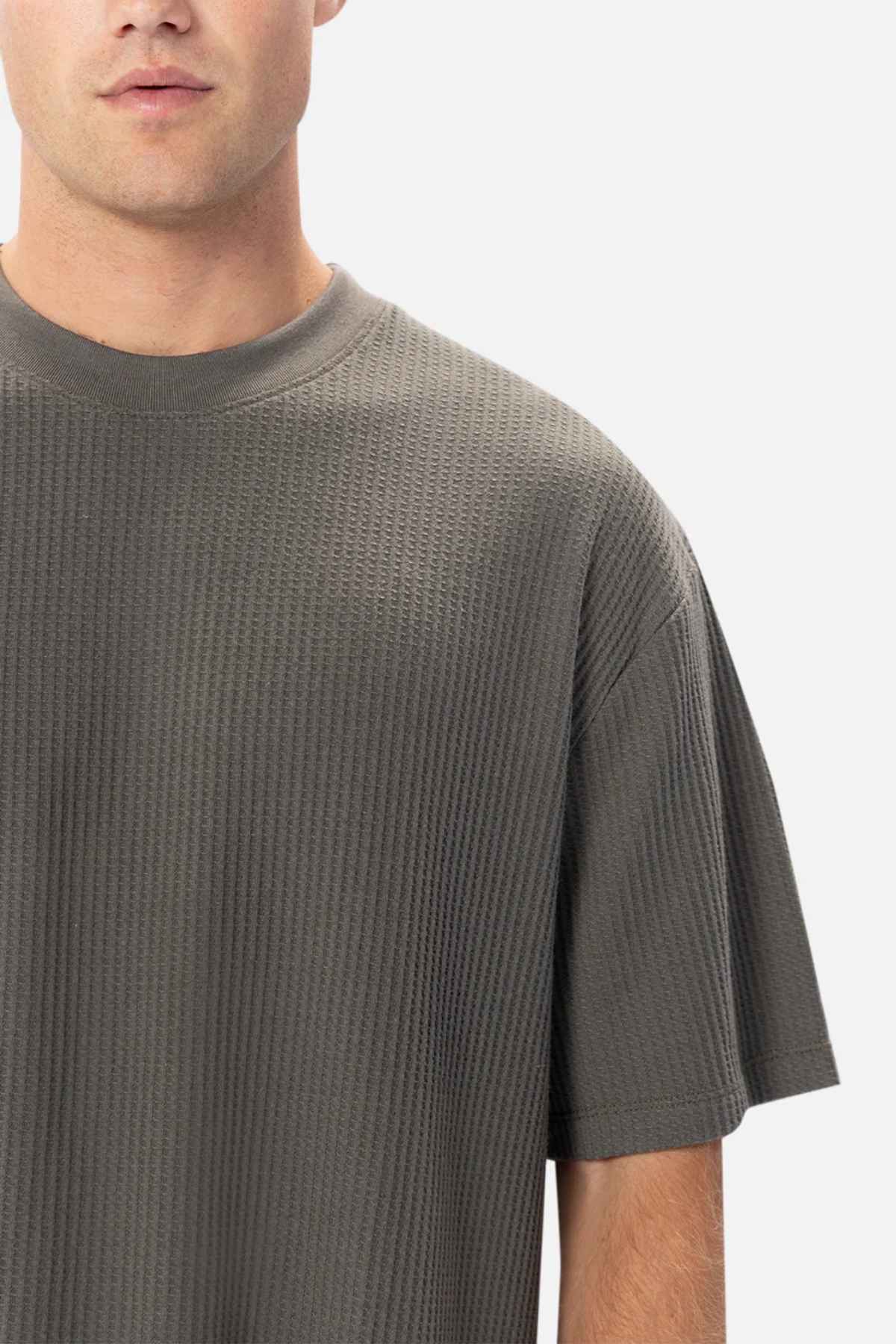 Close-up of a person wearing a textured, dark gray Industrie The Earl Waffle Tee with a classic crew neck, covering the upper left part of their body. The background is plain white, and the person's face is partially visible from the nose down.