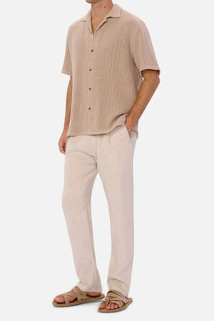 A man poses against a white backdrop in the Industrie Egnazia Short Sleeve Shirt, styled with cream linen-cotton blend pants for a summer look, completed by brown sandals.
