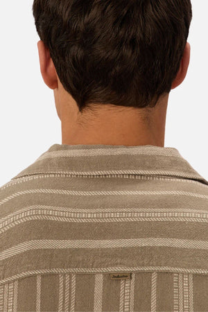 A close-up of the back of a person with short brown hair wearing the Industrie The Fabriano Short Sleeve Shirt in beige cotton, featuring white stripes, a relaxed fit, and a small "Industrie" label on the upper back.