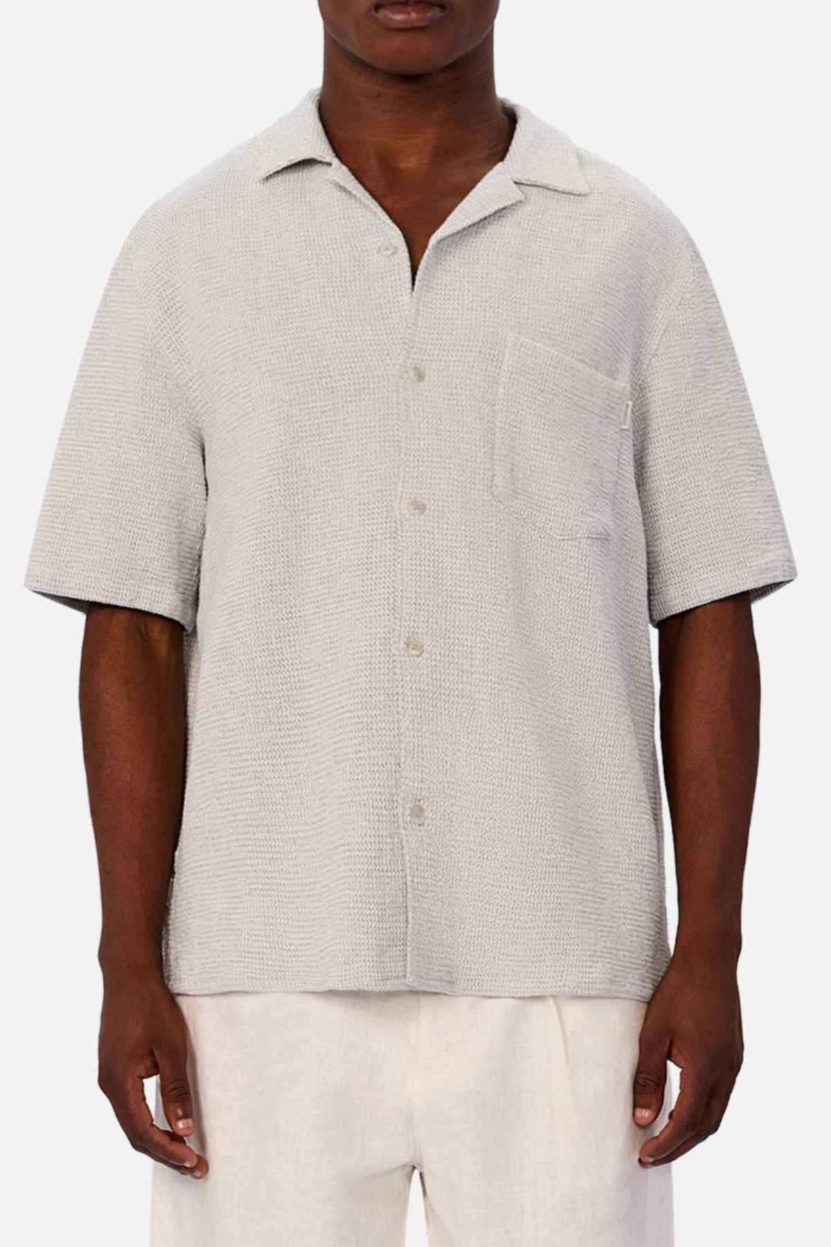 A person wears the Industrie The Franklin Short Sleeve Shirt—light gray, breathable cotton with a camp collar and chest pocket—paired with off-white pants, standing against a plain white background.