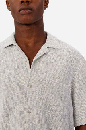 A person wears the Industrie The Franklin Short Sleeve Shirt, a light grey textured casual camp collar shirt with a front pocket, shown from shoulders to mid-chest against a plain white background.