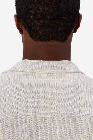 A person with short curly hair is shown from behind wearing the Industrie The Franklin Short Sleeve Shirt, a breathable cotton, casual camp collar style. A small "INDUSTRIE" tag is visible on the upper back of the shirt.