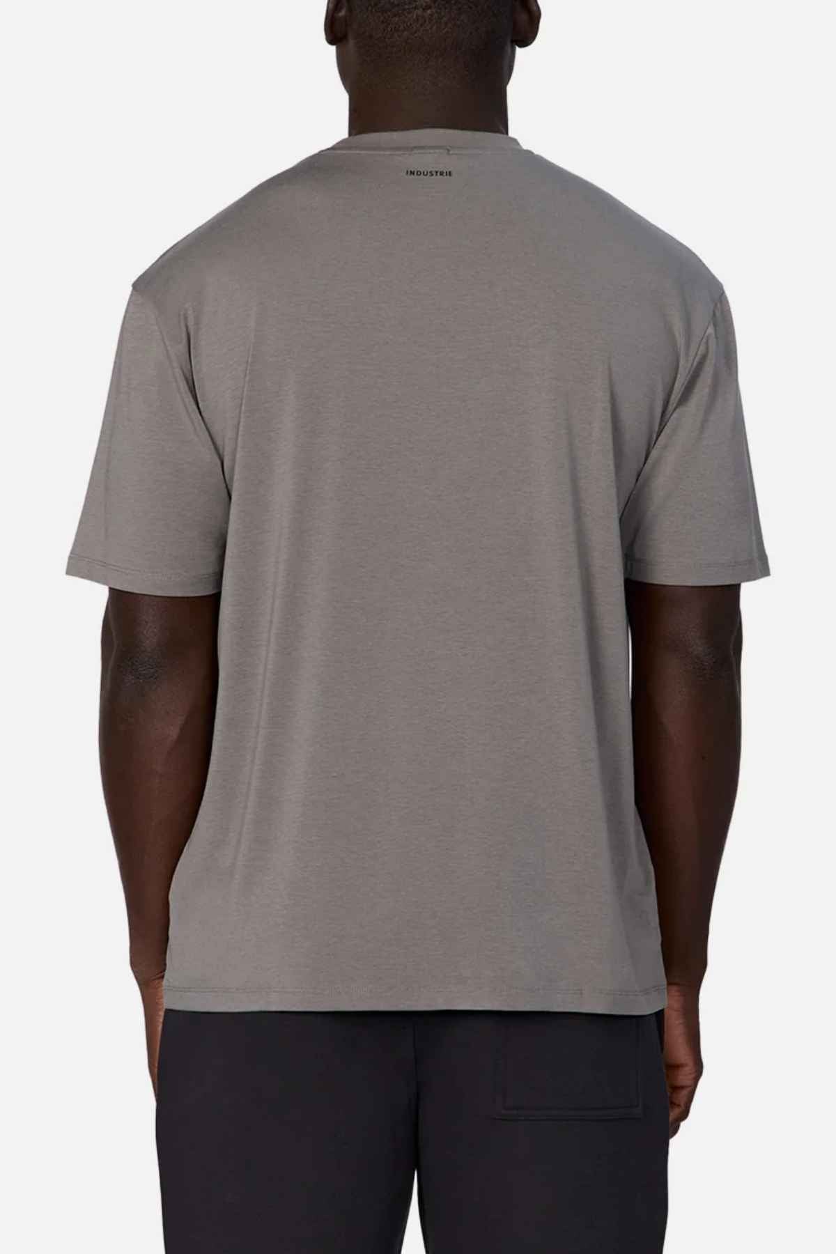 A person is shown from the back wearing a relaxed-fit gray Freeman Athletic Tee by Industrie, paired with black pants. The T-shirt displays the subtle Industrie branding with a small logo located at the top center near the neckline, set against a plain white background.