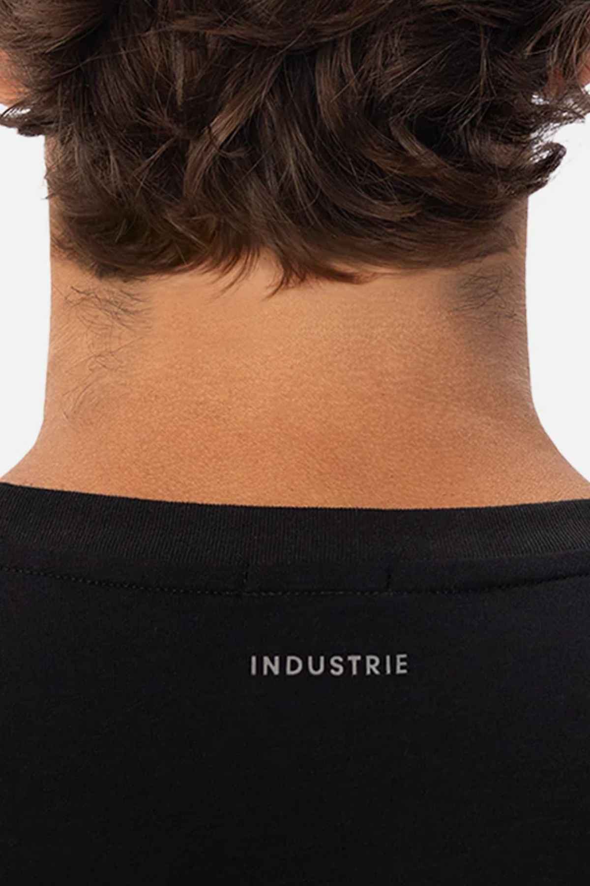 A close-up of the back of a person's neck and head highlights their dark brown hair and the upper portion of a black, relaxed-fit shirt. The word "INDUSTRIE" is elegantly printed in small white letters below the neckline, capturing the effortless style characteristic of Industrie The Freeman Athletic Tee.