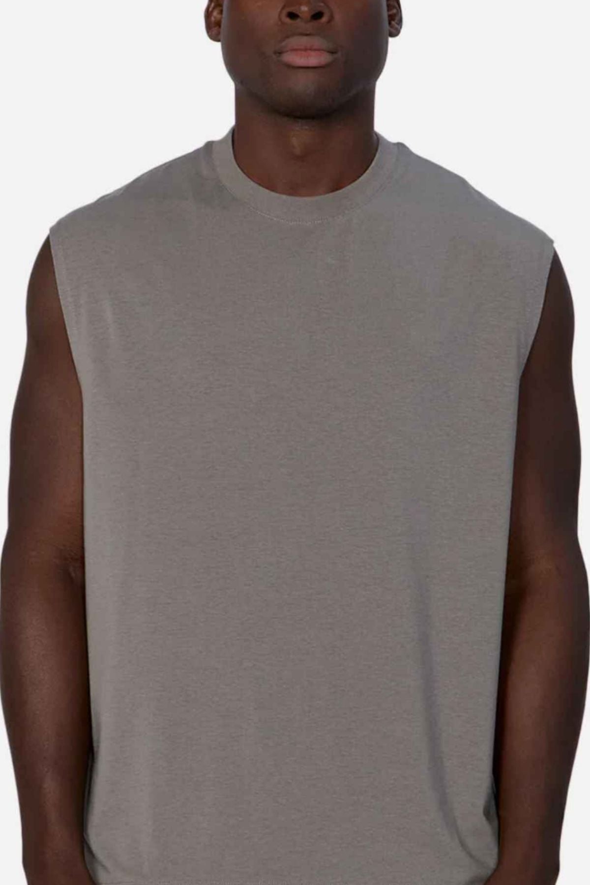 Wearing the Industrie The Freeman Sleeveless Tee, a person with dark skin poses against a plain light background. The cropped gray workout shirt reveals the upper torso and part of the face.