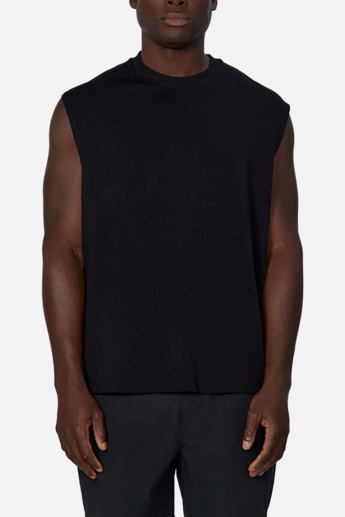A person wears the Industrie The Freeman Sleeveless Tee in black, paired with black pants, standing against a plain light background and facing forward with arms relaxed at their sides.